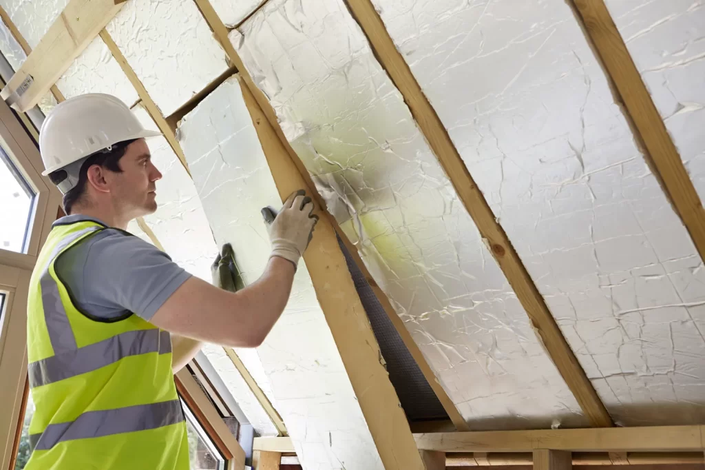 Installer fitting foil-faced rigid foam board insulation between attic rafters